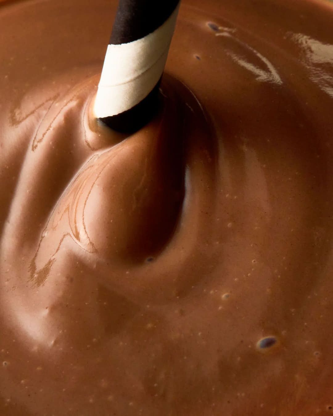 Close-up of swirling brown chocolate drink with a black and white striped paper straw; rich, creamy texture, and inviting dark brown tones.