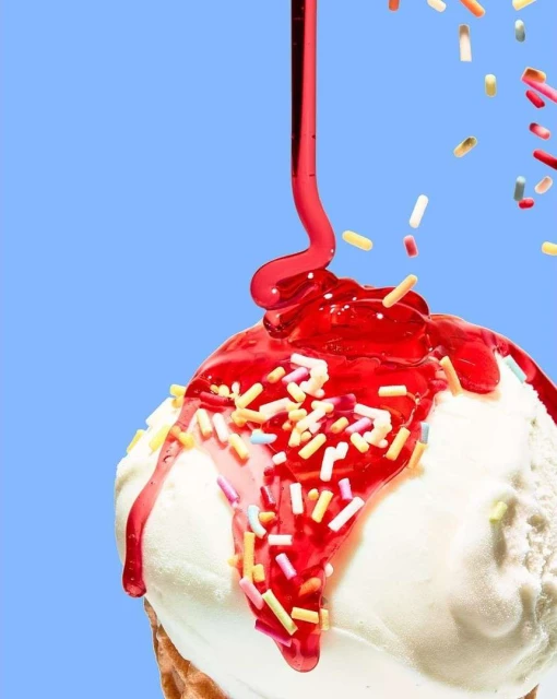 Ice cream cone with white ice cream and a red sauce drizzle with colorful sprinkles, studio shot against a solid light blue backdrop.