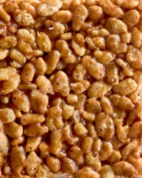 Macro close-up shot of crispy puffed rice cereal bound together in sticky amber caramel syrup.