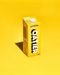 A yellow oat milk carton stands upright on a bright yellow seamless background, casting a sharp shadow to the left.