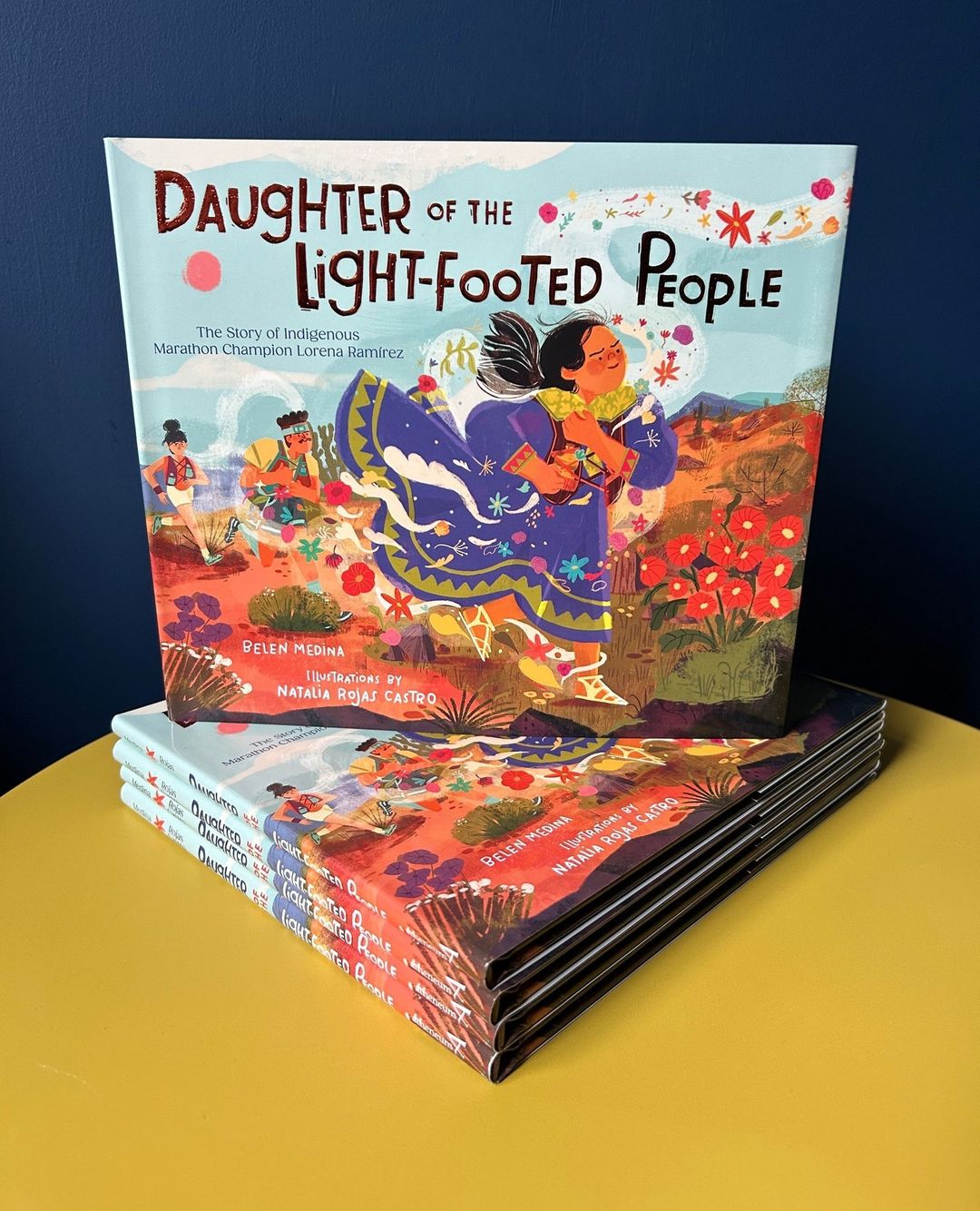 Book cover featuring an illustration titled 'Daughter of the Light-Footed People' stacked on other copies against a dark blue background.