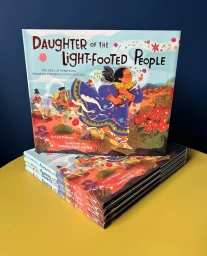 Children book titled Daughter of the Light-Footed People illustrated by Natalia Rojas Castro stacked on a yellow table