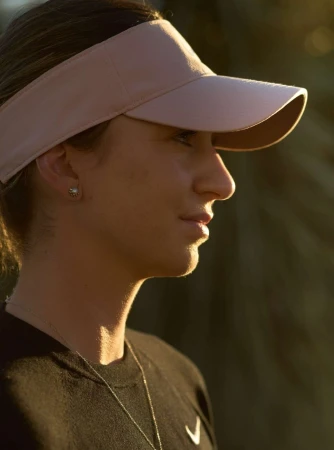 Profile portrait of a woman wearing a pink visor and black athletic t-shirt under warm natural sunlight, photographed in New York.