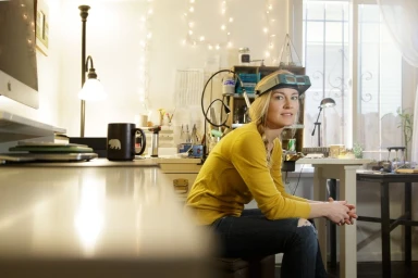 Woman wearing a yellow long-sleeve top and head magnifier sitting in a workshop, photographed by Natalie Faye.