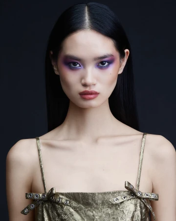 Portrait of an East Asian woman with long black hair, purple eye makeup, and metallic gold dress against a dark background by Natasja Fourie