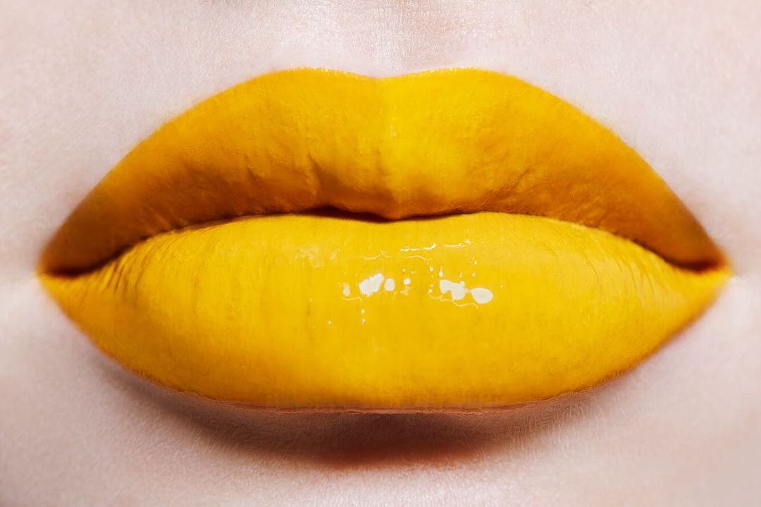 Close-up of a woman's lips painted with vibrant yellow lipstick and gloss, creating a striking and colorful beauty image.