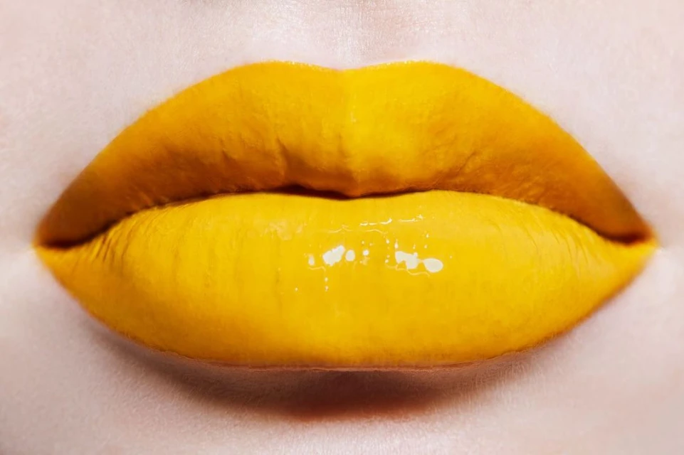 Close-up of a woman's lips painted with vibrant yellow lipstick and gloss, creating a striking and colorful beauty image.