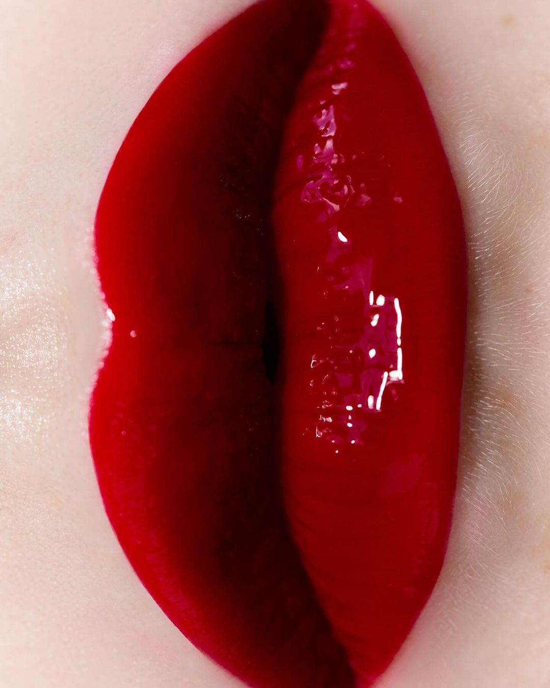 Close-up studio shot of red glossy lipstick on woman's lips, highlighting the texture and color in a beauty context.