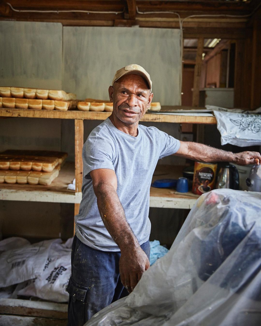 Portrait of a man in a cap standing inside a bakery with loaves of bread on shelves; a glimpse into the art of baking.