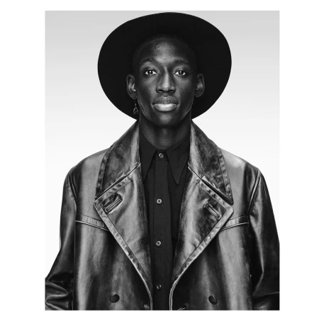Portrait of a black man wearing a wide-brimmed black hat, dark shirt, and leather coat against a white backdrop.