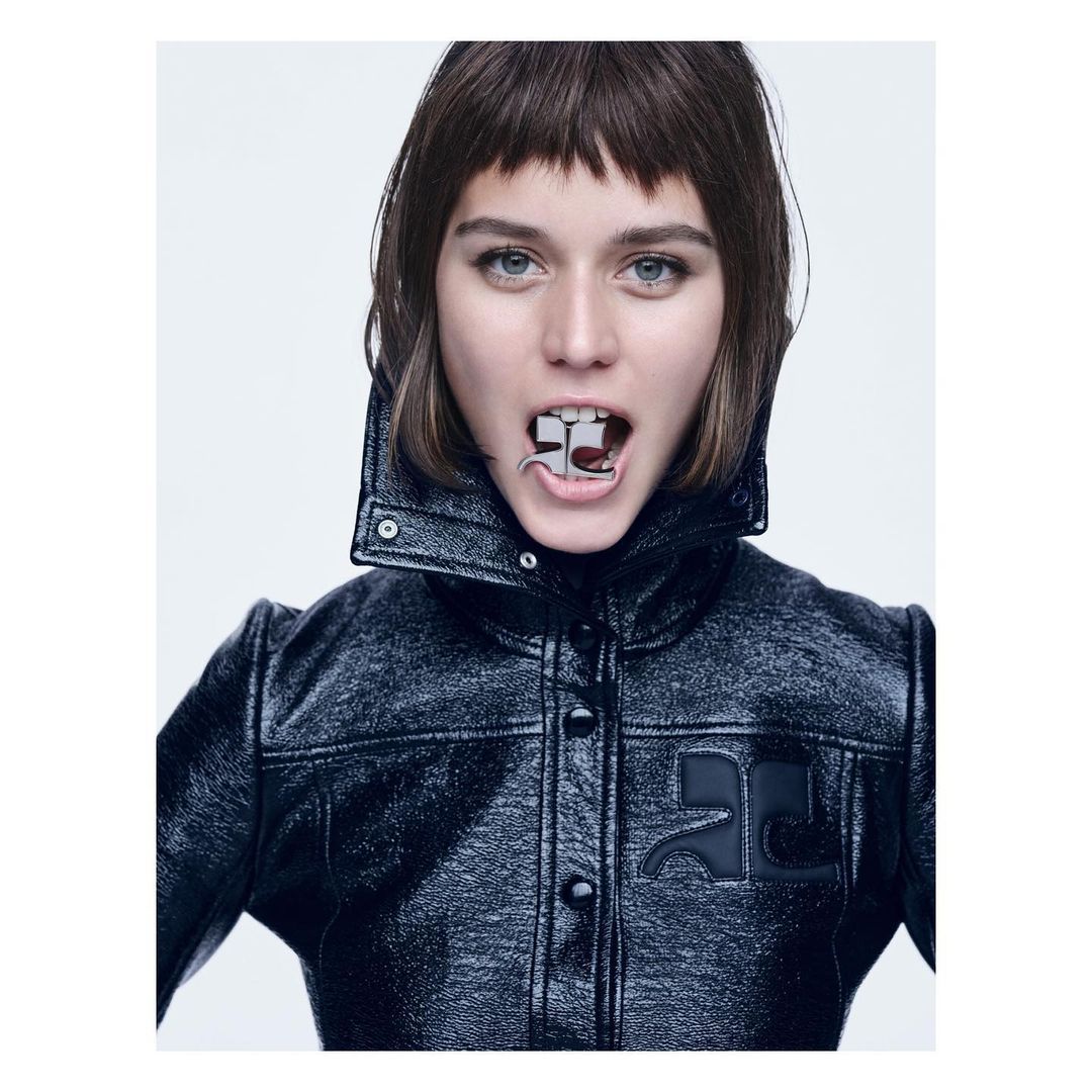 Glamorous portrait of a woman with dark hair and blue eyes wearing a black leather jacket, holding a metal dental tool in her mouth.