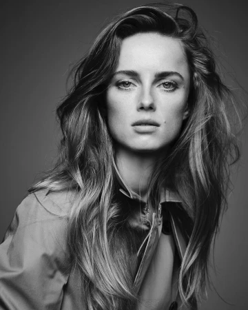 Portrait of a woman with long tousled hair wearing a buttoned jacket against a plain dark background