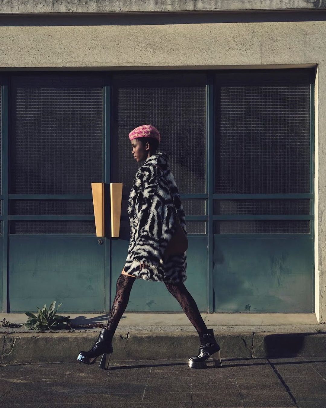 Model in zebra-print coat and pink beret walking past dark framed glass doors in Paris captured by Nathaniel Goldberg