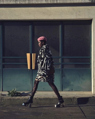 Model in zebra-print coat and pink beret walking past dark framed glass doors in Paris captured by Nathaniel Goldberg
