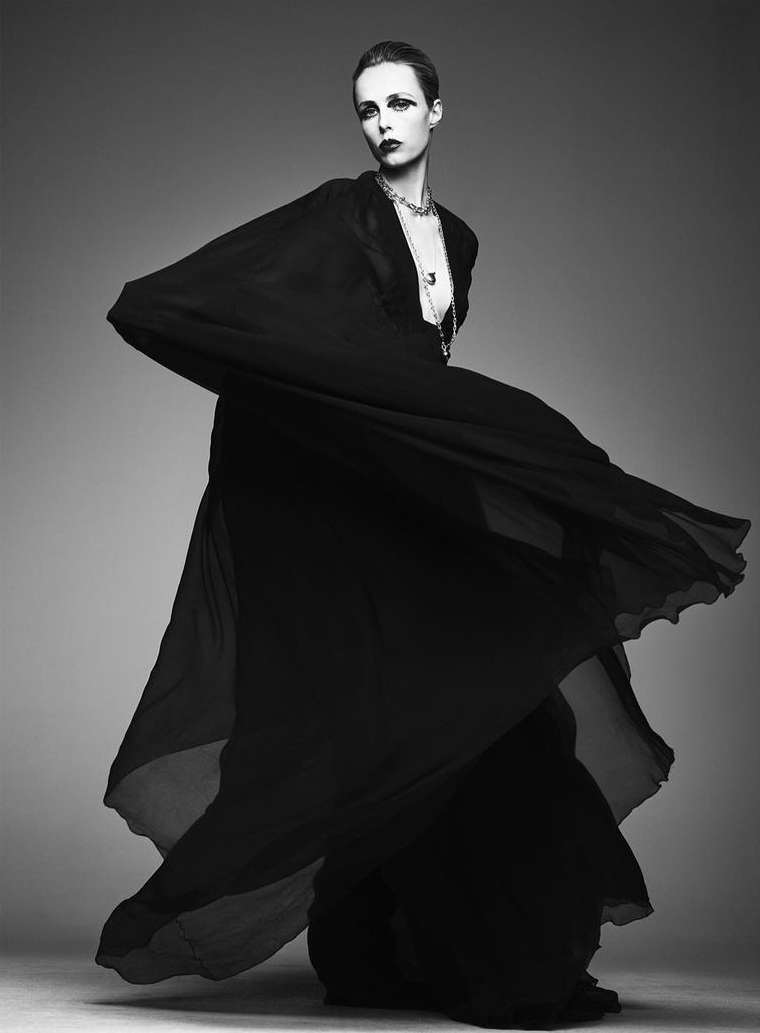 Elegant woman in black dress posing in a studio. Black and white fashion photograph featuring draped clothing and stylish female model.