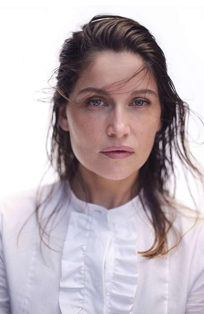 Headshot of an adult woman with dark hair wearing a white collared shirt against a bright background in a portrait-style composition.