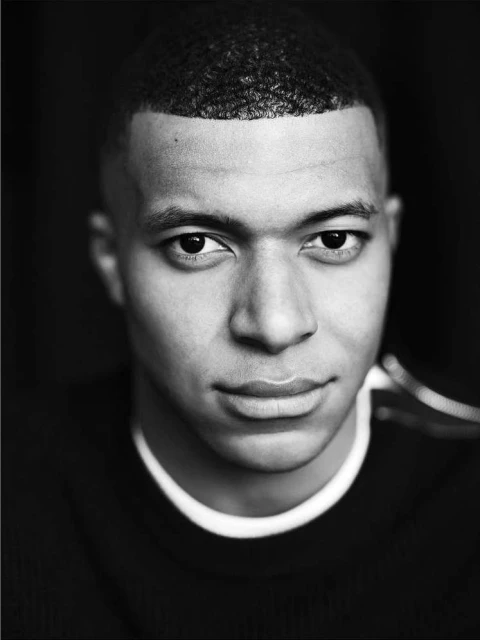 Close-up portrait of an adult male with short curly hair, wearing a crewneck shirt, in a black and white studio shot.
