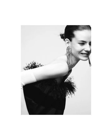 Black and white portrait of a smiling woman wearing feathered dress and crystal fringe earrings by photographer Nathaniel Goldberg.