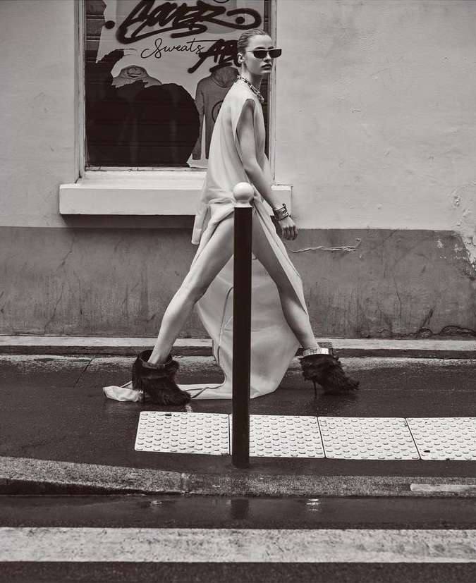 Model in sunglasses and flowing dress walking past a street bollard in Paris by Nathaniel Goldberg