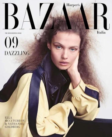 Model with voluminous hair wearing a yellow and navy jacket against a plain background