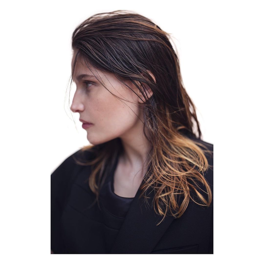 Profile shot of a woman with wet, dark hair, wearing a black jacket against a white backdrop. Beauty and fashion portrait.