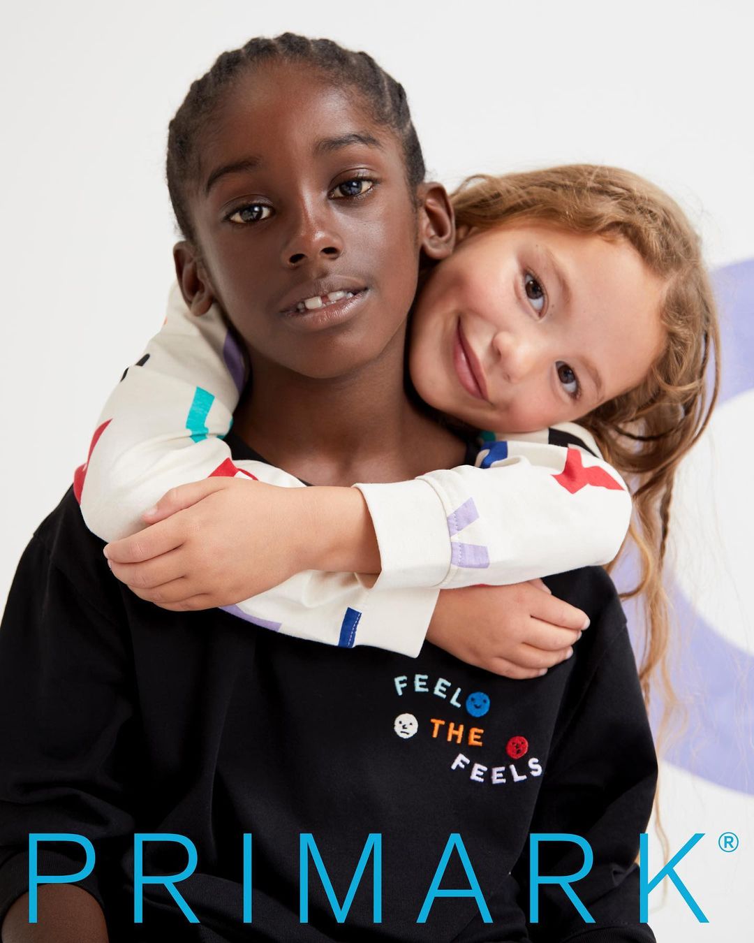 Two young children embracing while looking at the camera in a fashion campaign for Primark, shot with natural lighting.