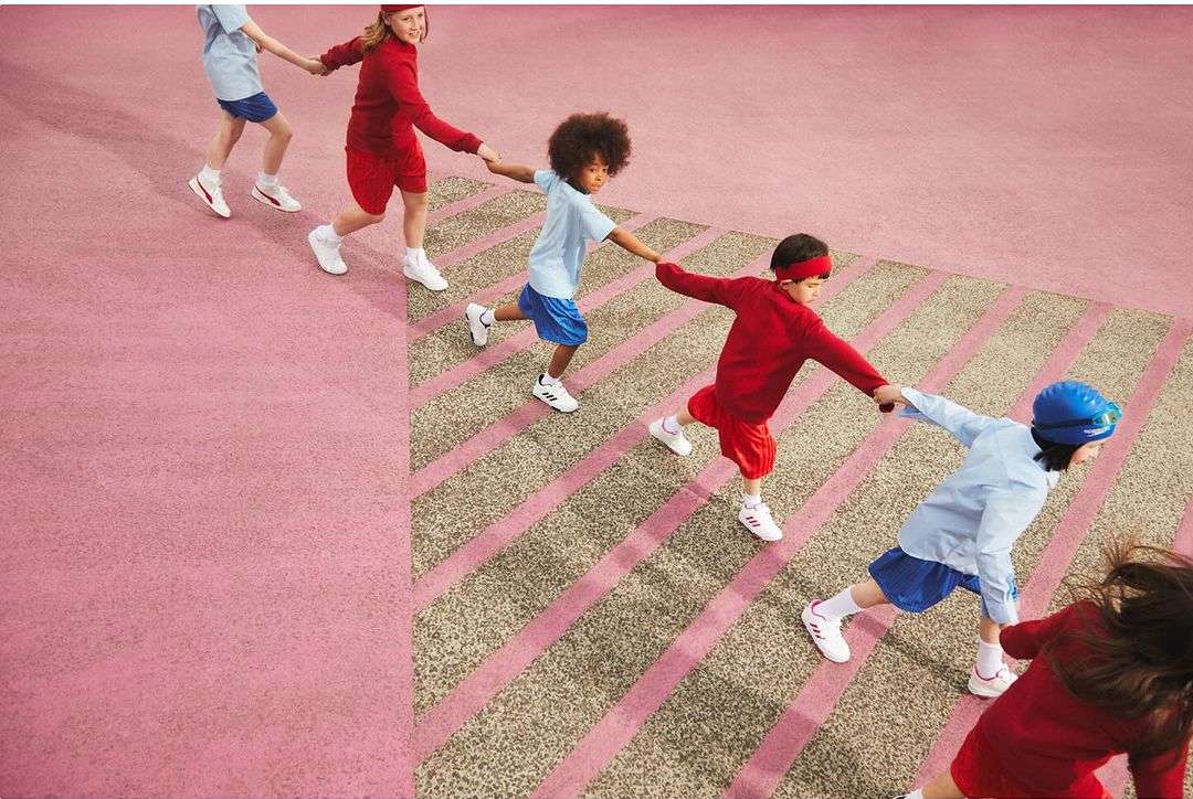 Kids in red and blue athletic wear holding hands and walking on a light pink and tan patterned surface in an overhead shot.