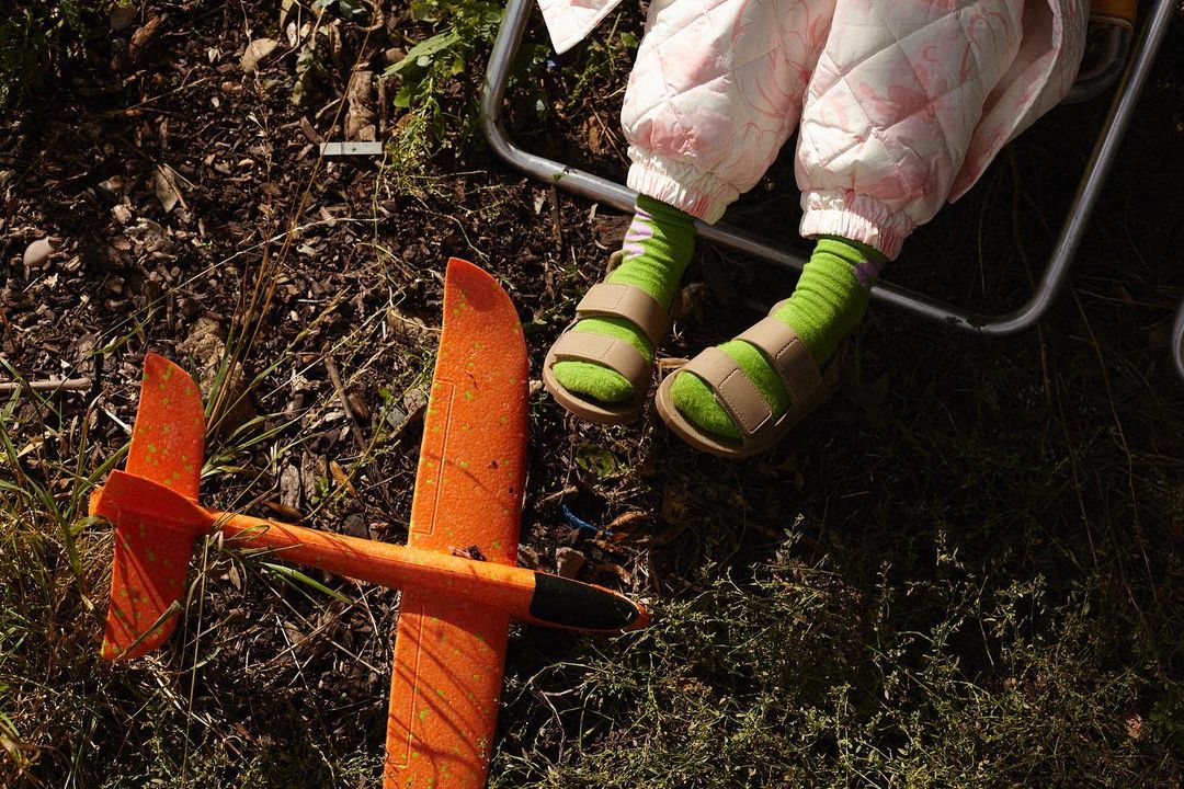 Child's legs and feet in sandals with a toy airplane on the ground outdoors, showing a playful and relaxed scene.