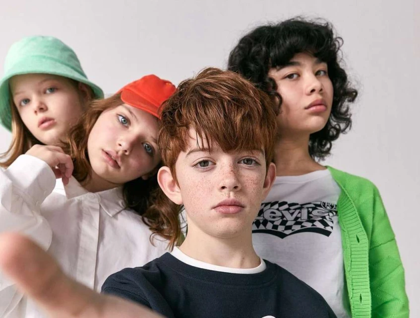 Four young children pose in a photo studio. Two are wearing hats and colorful tops in this eye-level medium shot with a white backdrop.