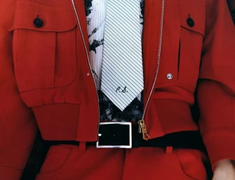 Close-up of a person wearing a bright red utility jacket, striped necktie, and black belt with silver buckle.