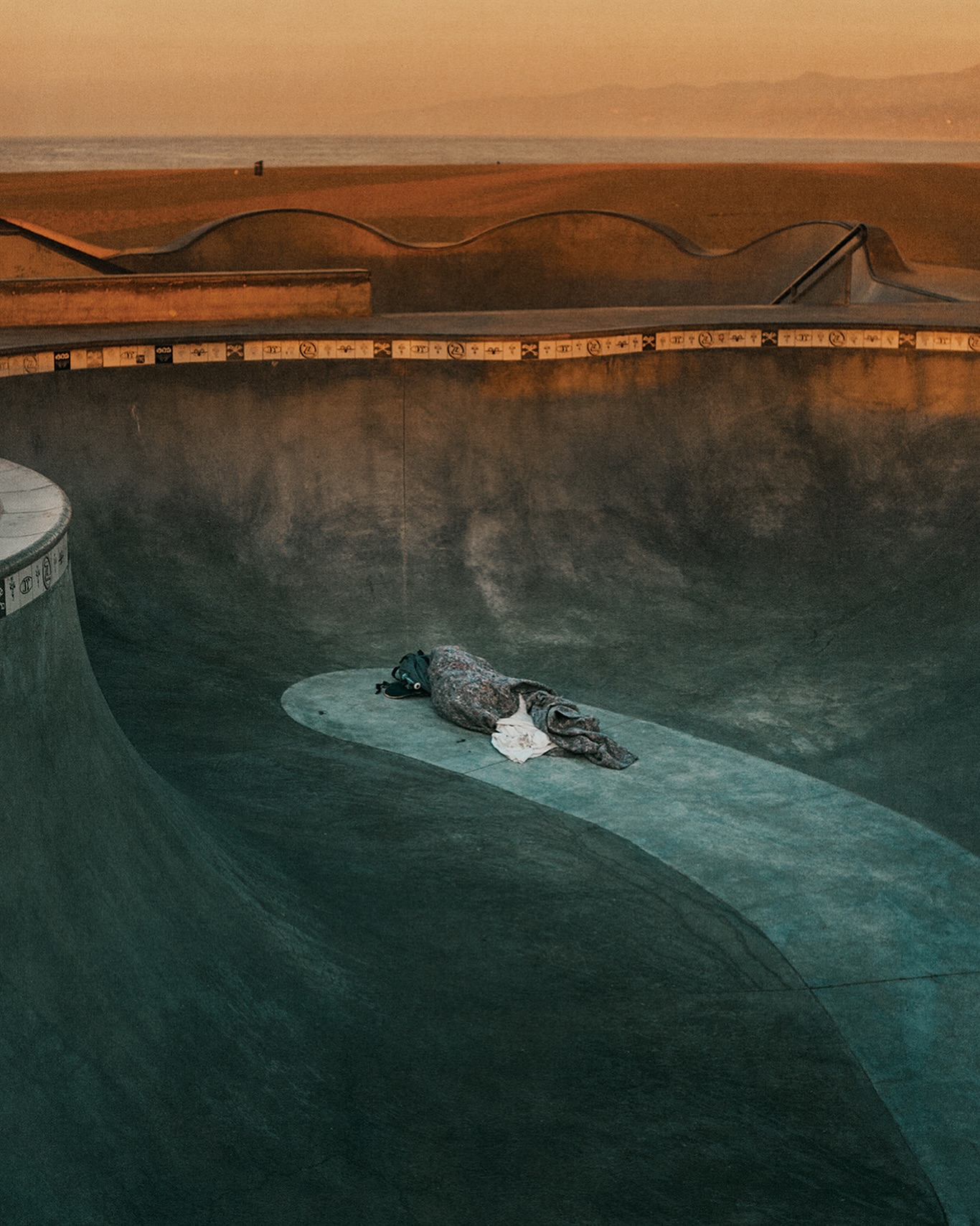 Empty skatepark bowl at golden hour, with concrete ramps, an abandoned object and horizon in the distance. Great for urban sports.