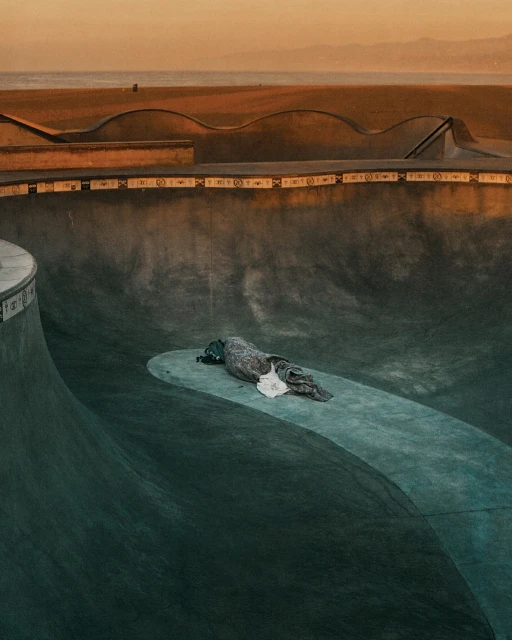 Empty skatepark bowl at golden hour, with concrete ramps, an abandoned object and horizon in the distance. Great for urban sports.