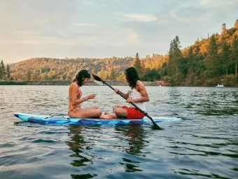 Man and woman sitting on a blue paddleboard in the middle of a lake holding a paddle, captured by Niall OBrien.