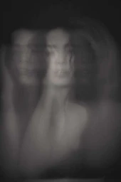 Portrait of a woman captured with motion blur and multiple exposures against a dark background by Niall O’brien