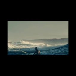 Surfer sitting on a surfboard in rolling ocean waves under an overcast sky, captured by Niall OBrien.