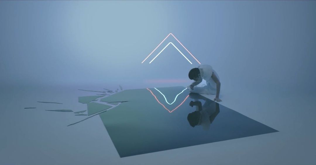 A slender adult in white reaches toward a reflective surface under neon lights against a stark white studio background.
