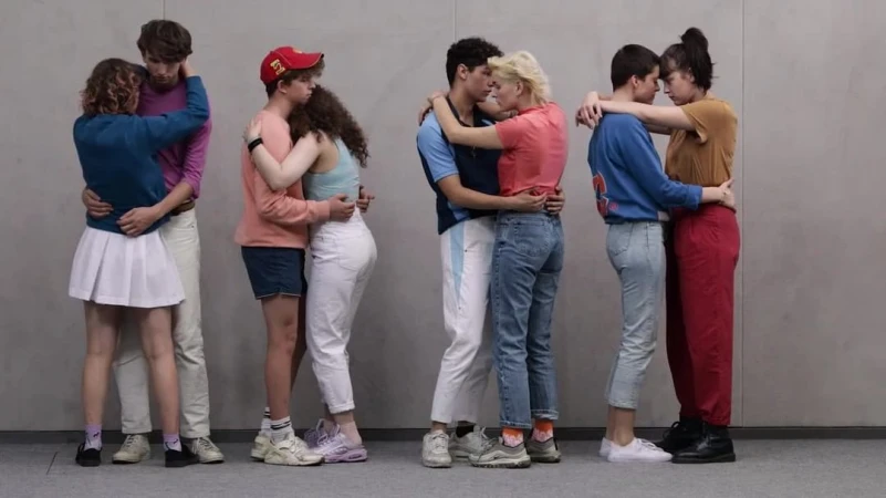 Four diverse young couples embrace in a row in casual streetwear against a neutral grey wall, highlighting connection and youthful relationships.