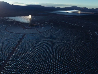 Aerial view of a massive solar thermal power plant featuring concentric rings of heliostat mirrors surrounding a central receiver tower in a desert.