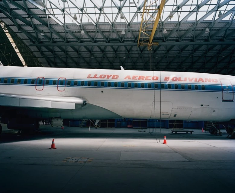 Side view of a Lloyd Aereo Boliviano aircraft parked in an airplane hangar, with orange traffic cones visible on the concrete floor.