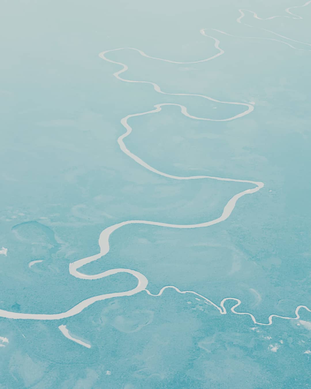 Aerial view of a winding river snaking through a light blue landscape, creating a pattern of curves and bends.