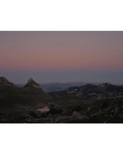 Scenic mountain range landscape view at dusk, featuring rocky terrain, distant peaks, and a soft, gradient sky from blue to pink.