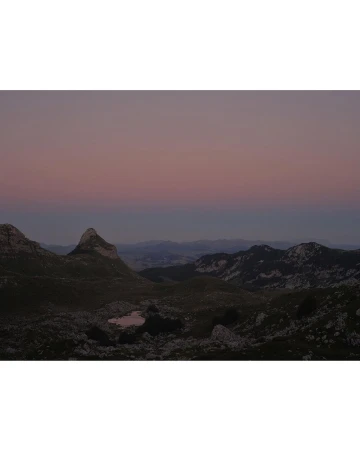 Scenic mountain range landscape view at dusk, featuring rocky terrain, distant peaks, and a soft, gradient sky from blue to pink.