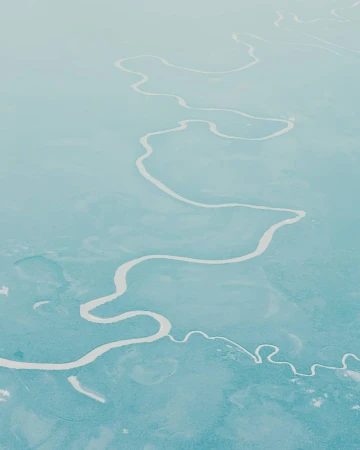 Aerial view of a winding river cutting through a vast, pale turquoise landscape.