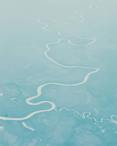 Aerial view of a winding river cutting through a vast, pale turquoise landscape.