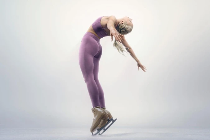 Female figure skater gracefully arches backward on ice, showcasing athletic skill in sportswear against a soft, diffused background.