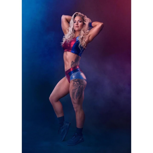 Fit female athlete in red and blue sportswear poses with hands behind her head in a studio with red and blue lighting.