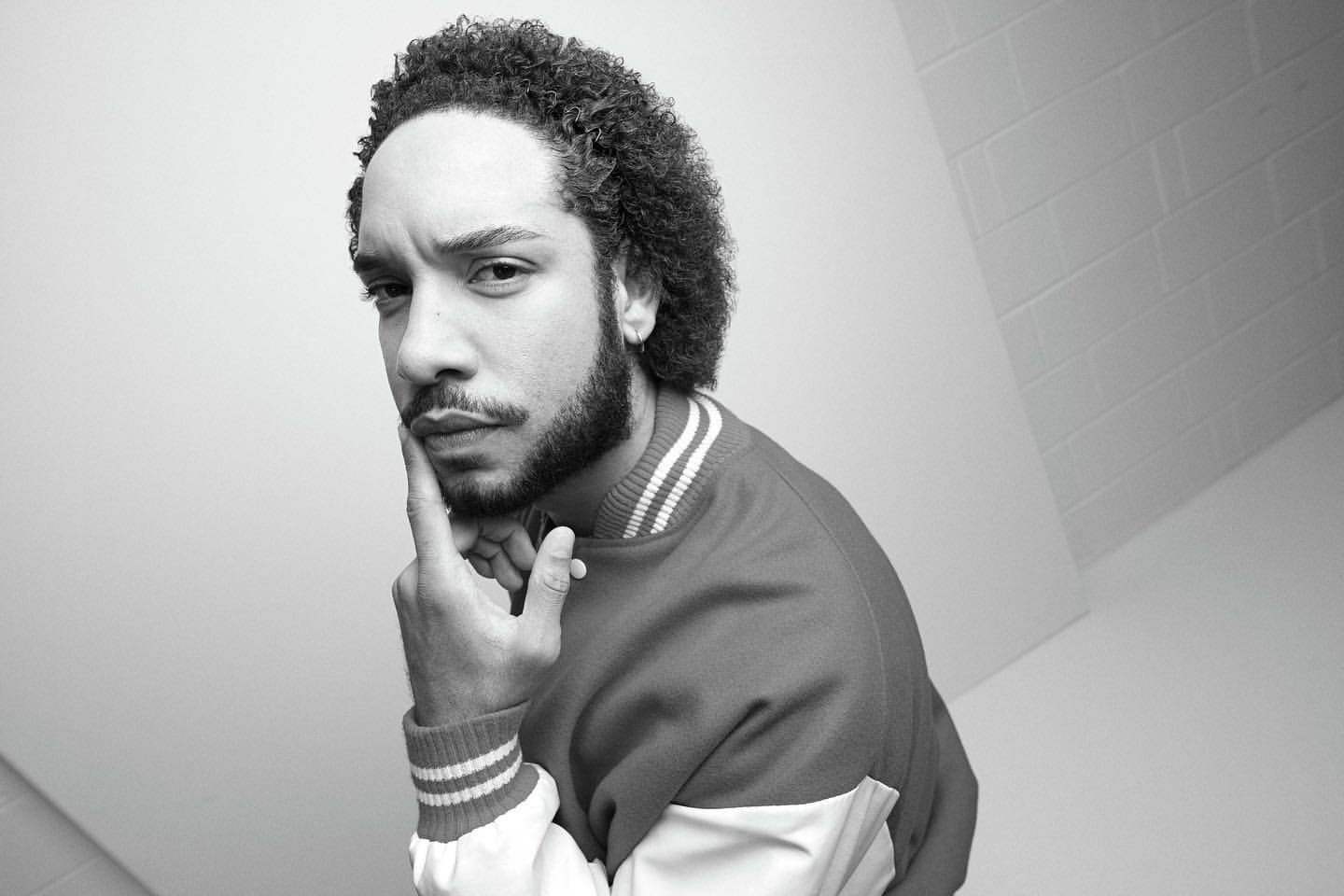 Portrait of a man with curly hair and a beard wearing a varsity jacket, photographed by Nick Eagle.
