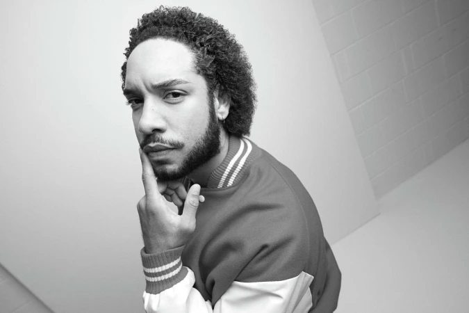 Portrait of a man with curly hair and a beard wearing a varsity jacket, photographed by Nick Eagle.