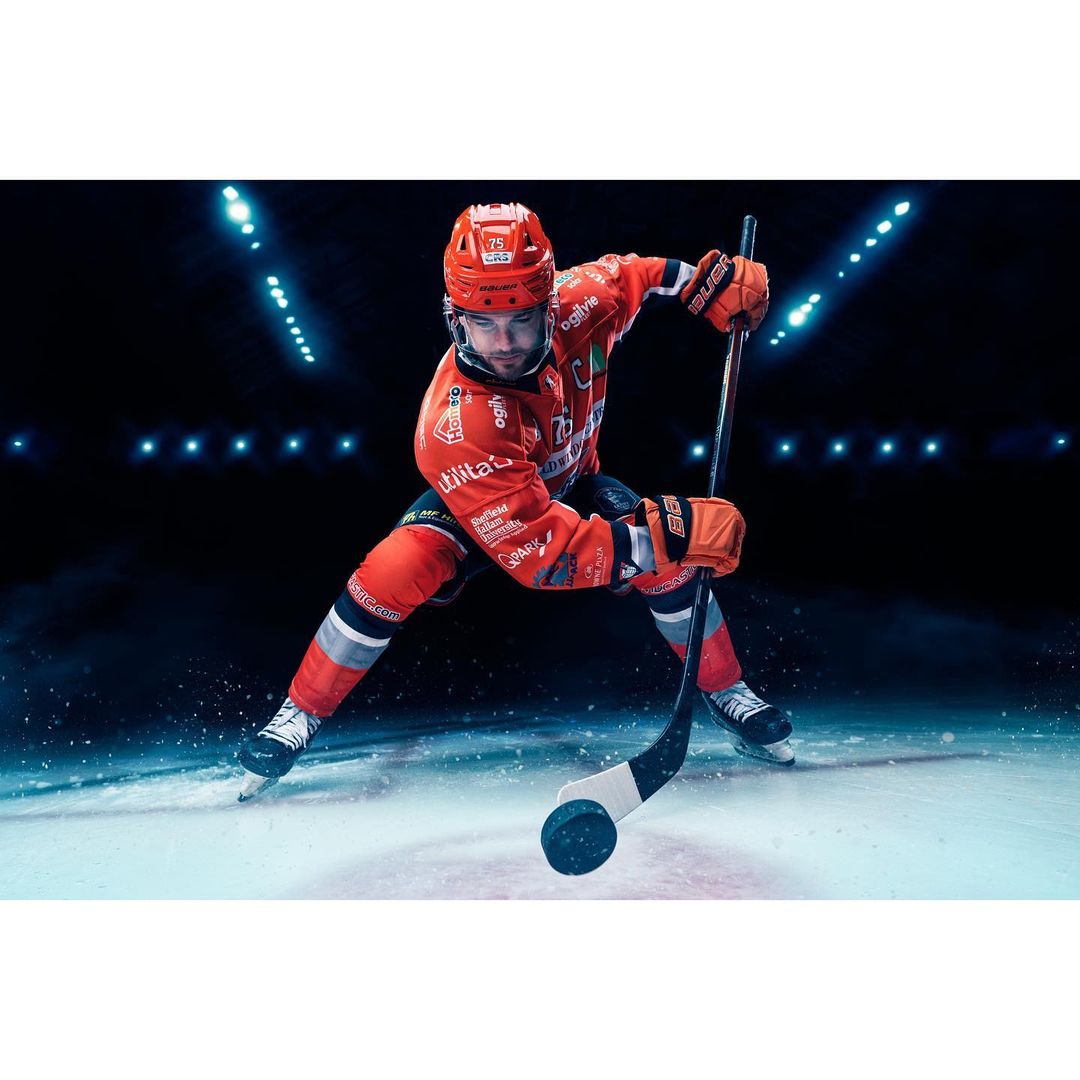 Hockey player in orange uniform with stick on ice rink under stadium lights. Action shot of sportsperson during a hockey game.