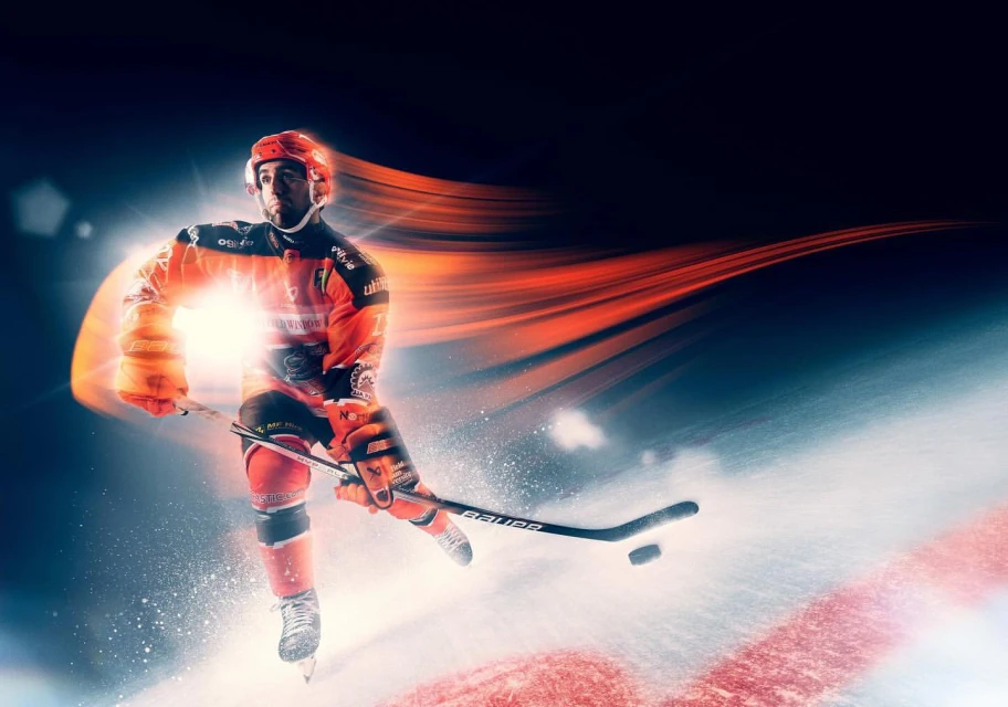 Dynamic action shot of a hockey player in orange uniform skating on ice with streaks of light and motion blur. Sport and energy.